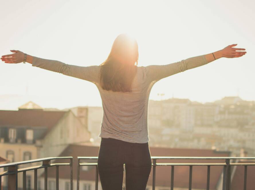 A woman stands with outstretched arms on a sunny balcony, embracing the morning light.