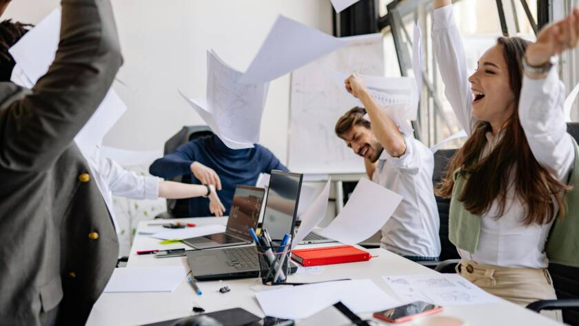 Group of diverse business professionals celebrating success in a modern office setting.